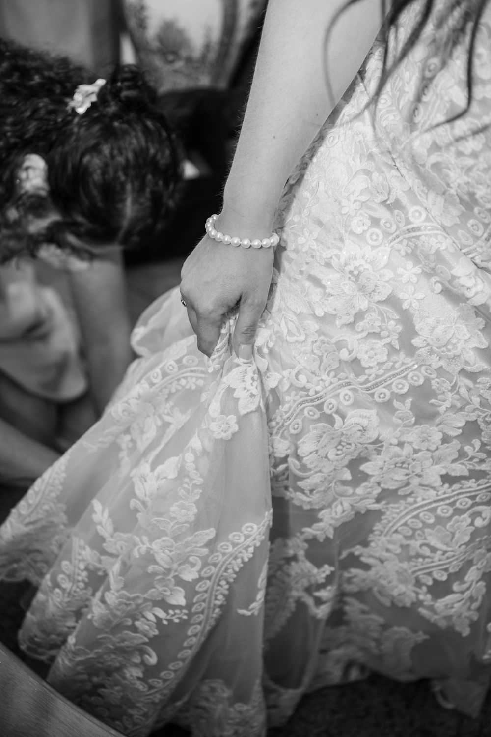 Close-up detail of a delicate lace wedding dress with pearl bracelet accent.
