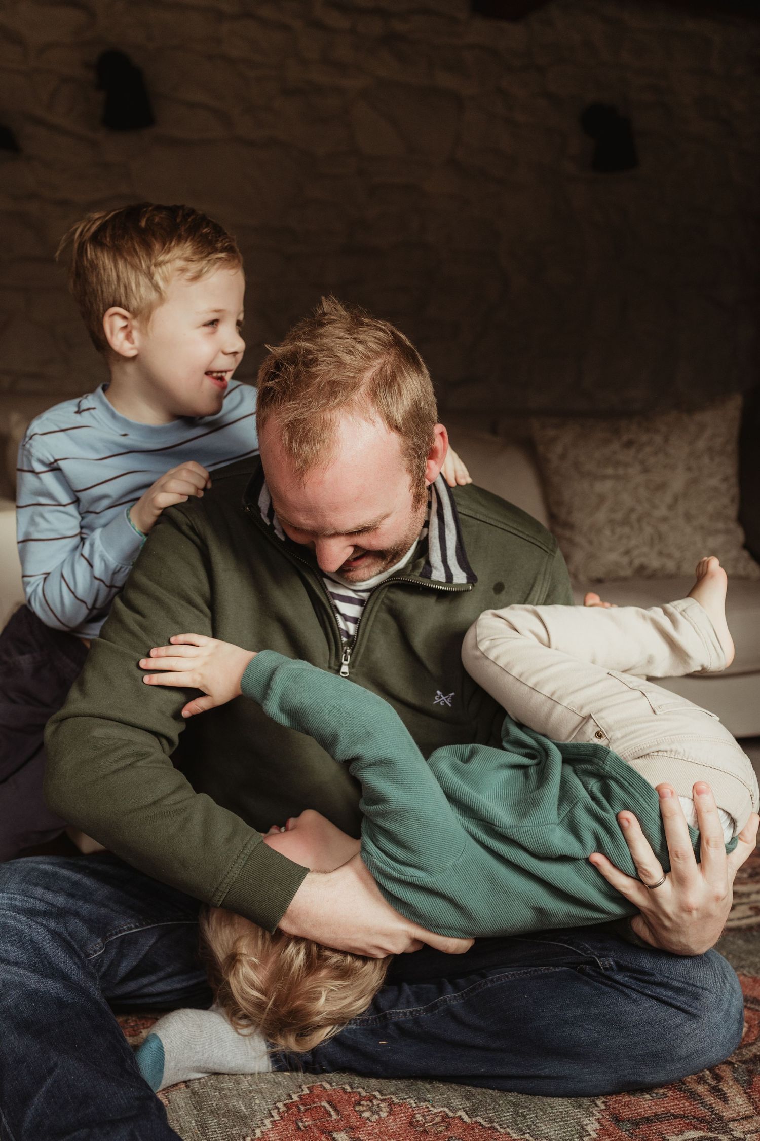 Indoor portrait of parent and baby sitting together on patterned rug in natural light.
