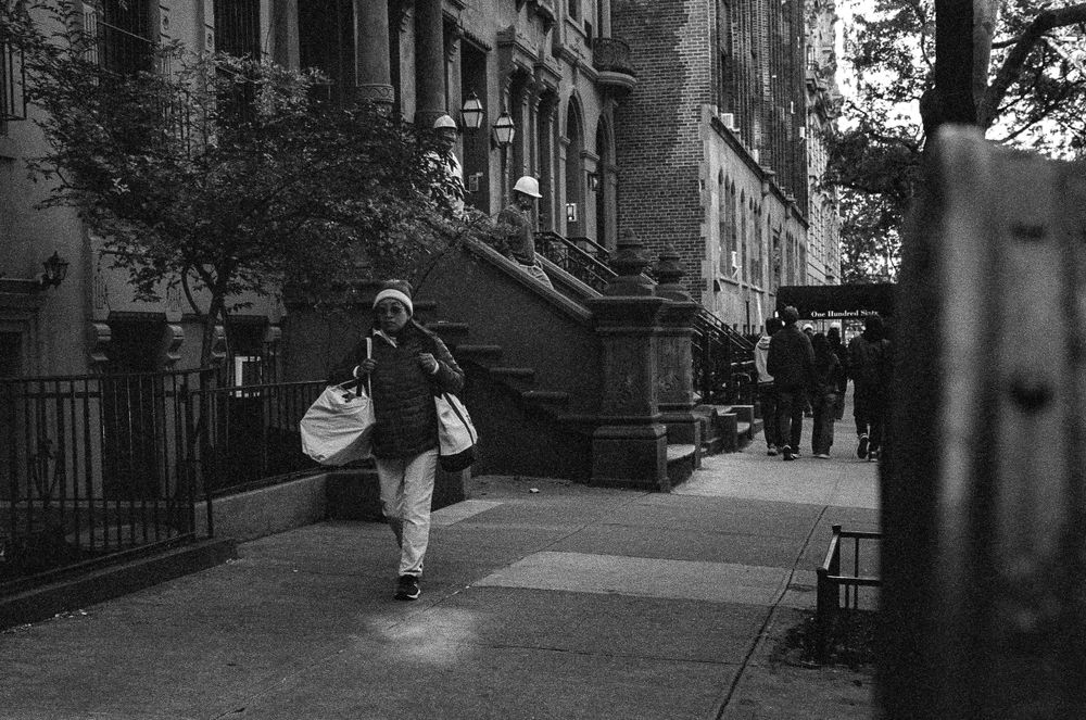 Person walking on a brownstone-lined street carrying shopping bags.