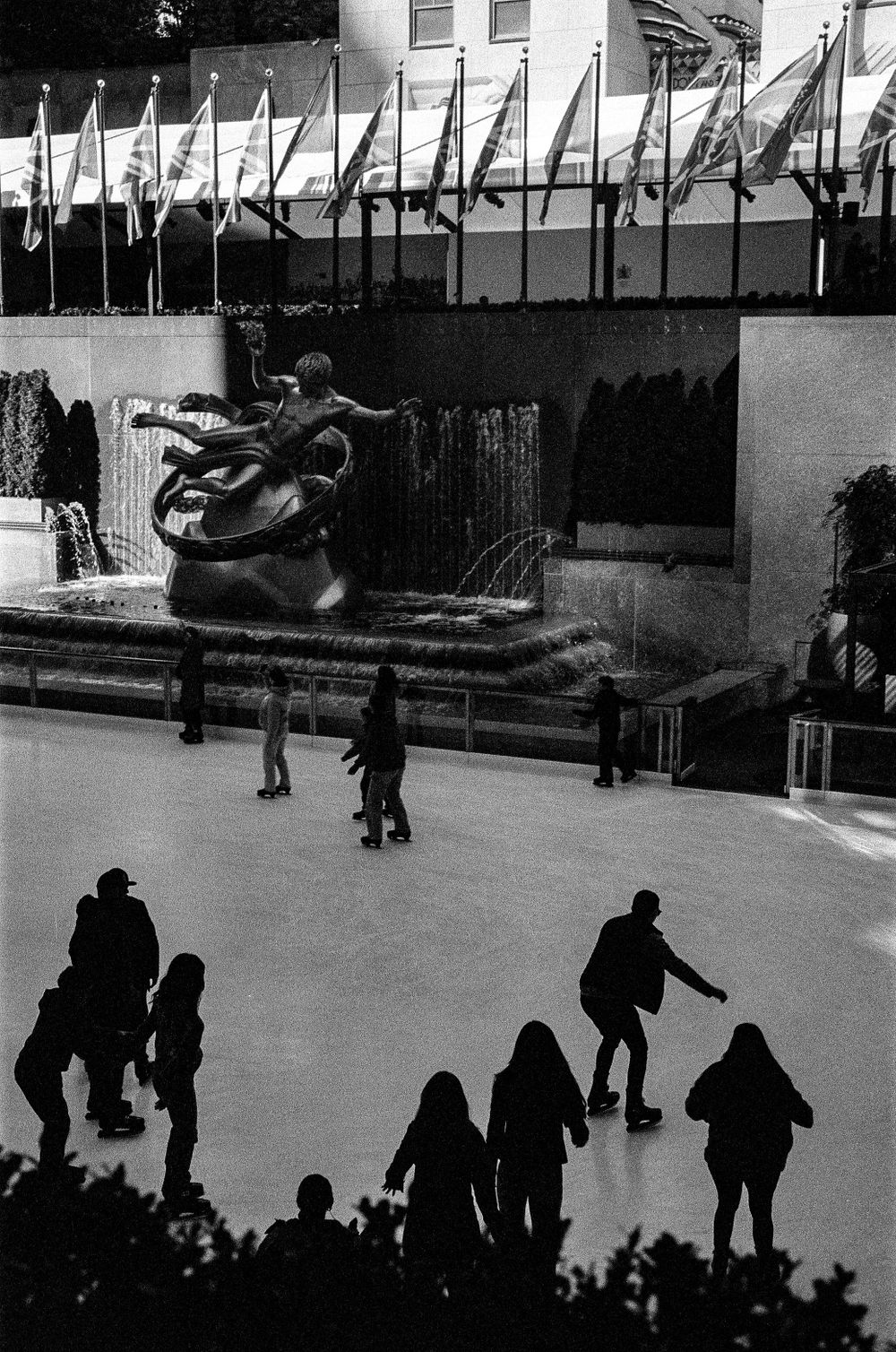 Ice skaters gliding on a rink beneath rows of flags.