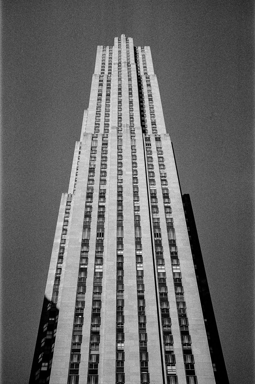 Looking up at the iconic art deco Rockefeller Center building in black and white.