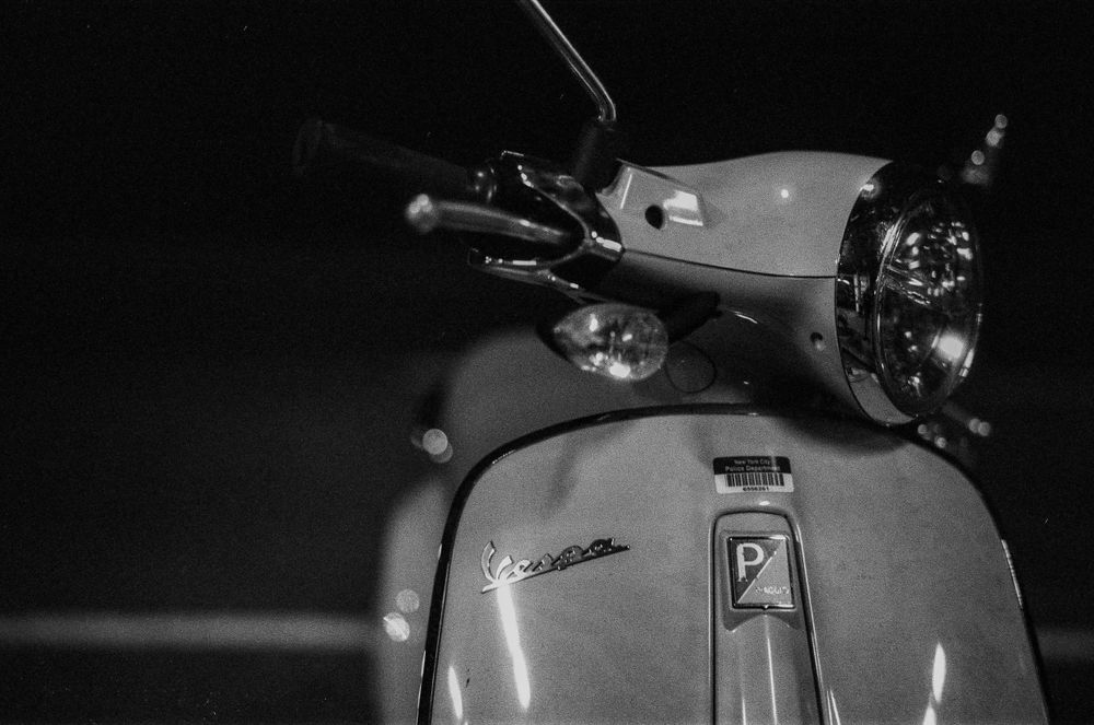 Close-up detail of a vintage Vespa scooter headlight and handlebars.