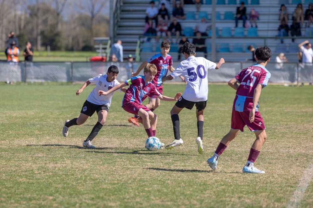 Soccer match action with players in purple and white uniforms battling for ball control.