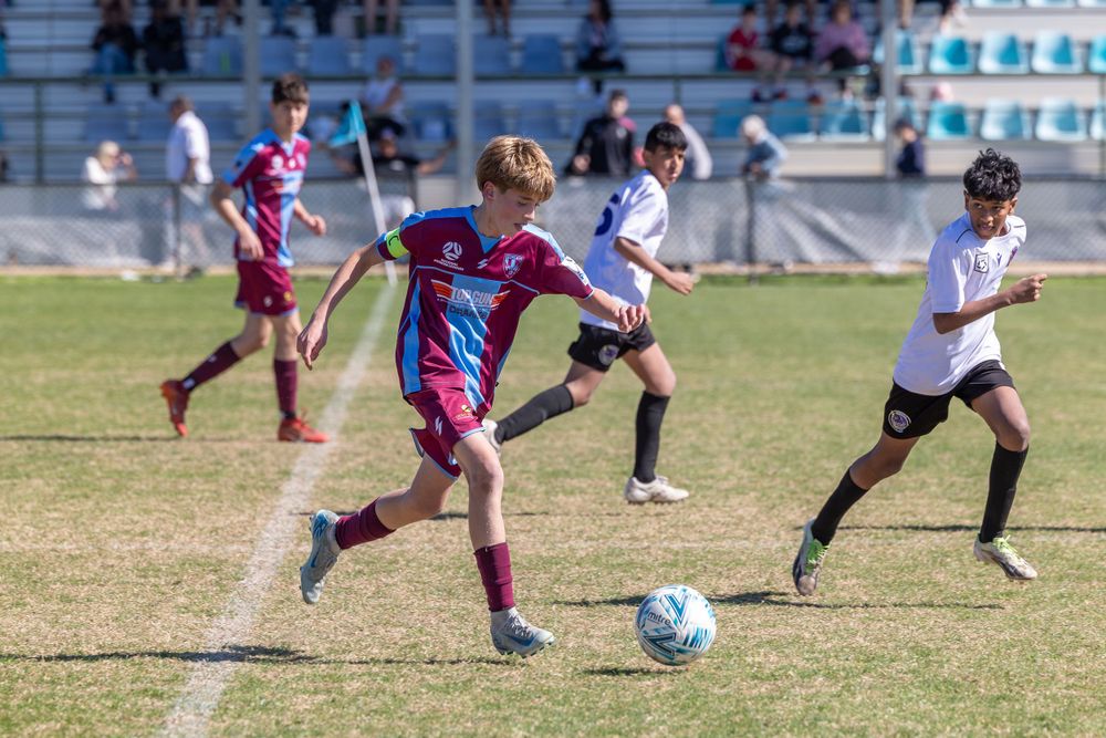 Soccer player in maroon and blue stripes dribbles ball during competitive match.