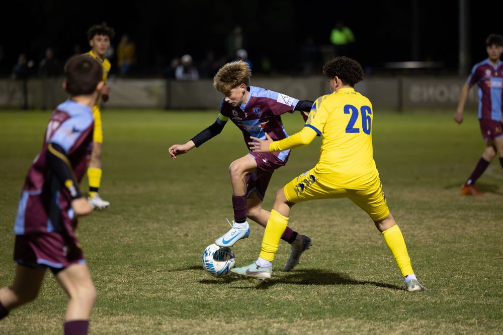 Soccer players competing for ball control during nighttime match between maroon and yellow teams.