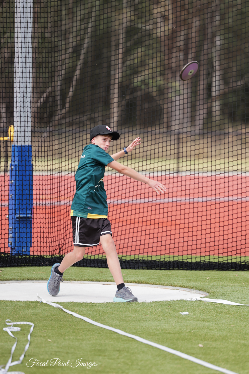 Athlete in green uniform throws discus during track and field competition.
