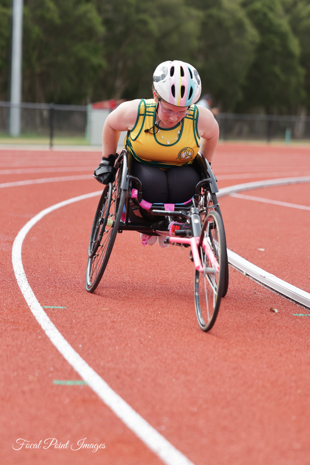 Wheelchair athlete in yellow singlet races on red running track during competition.