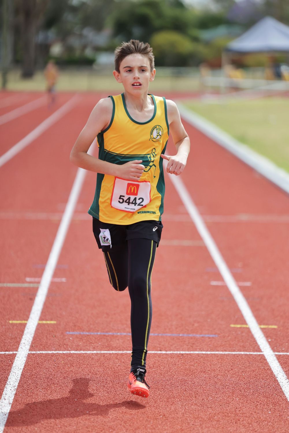 Track athlete in yellow singlet runs on red racing track during competition.
