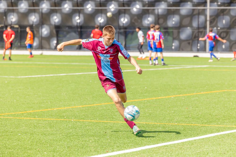 Soccer player in red and blue striped jersey kicks ball during game.