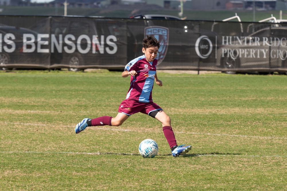 Soccer player in maroon and blue uniform kicking ball on sports field.