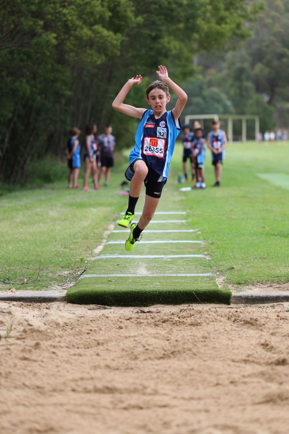 Young athlete performing a long jump drill on training squares outdoors.