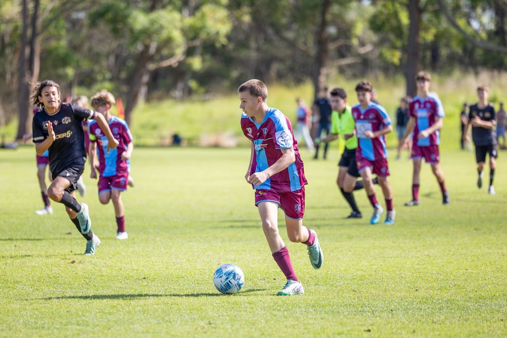 Soccer players in purple and red striped jerseys compete on a sunny grass field.