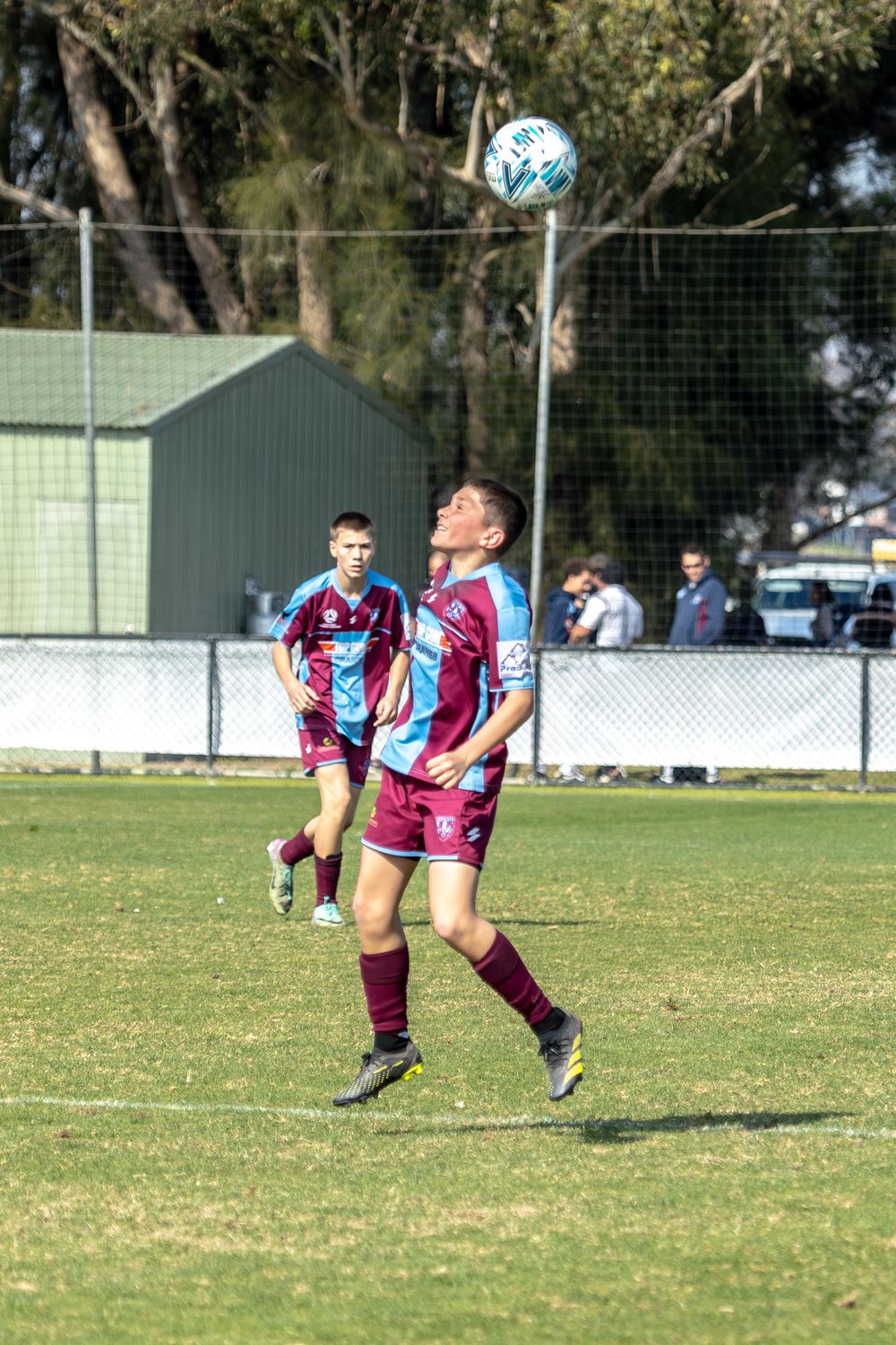 Soccer player in claret and light blue uniform jumps to head the ball during a match.