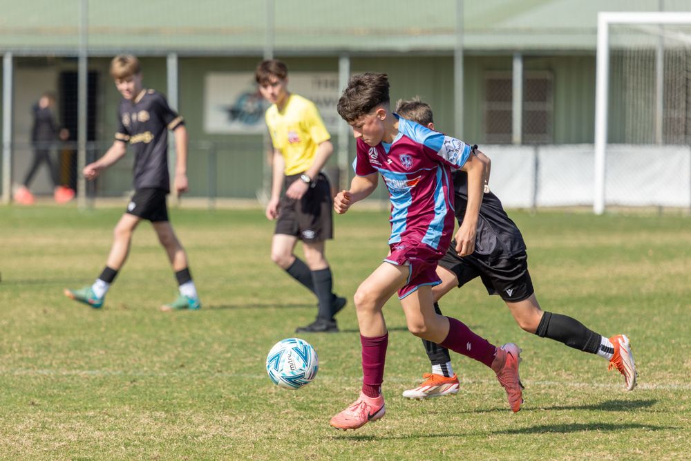 Soccer players in claret and blue jerseys compete for possession of the ball on a sunny grass field.