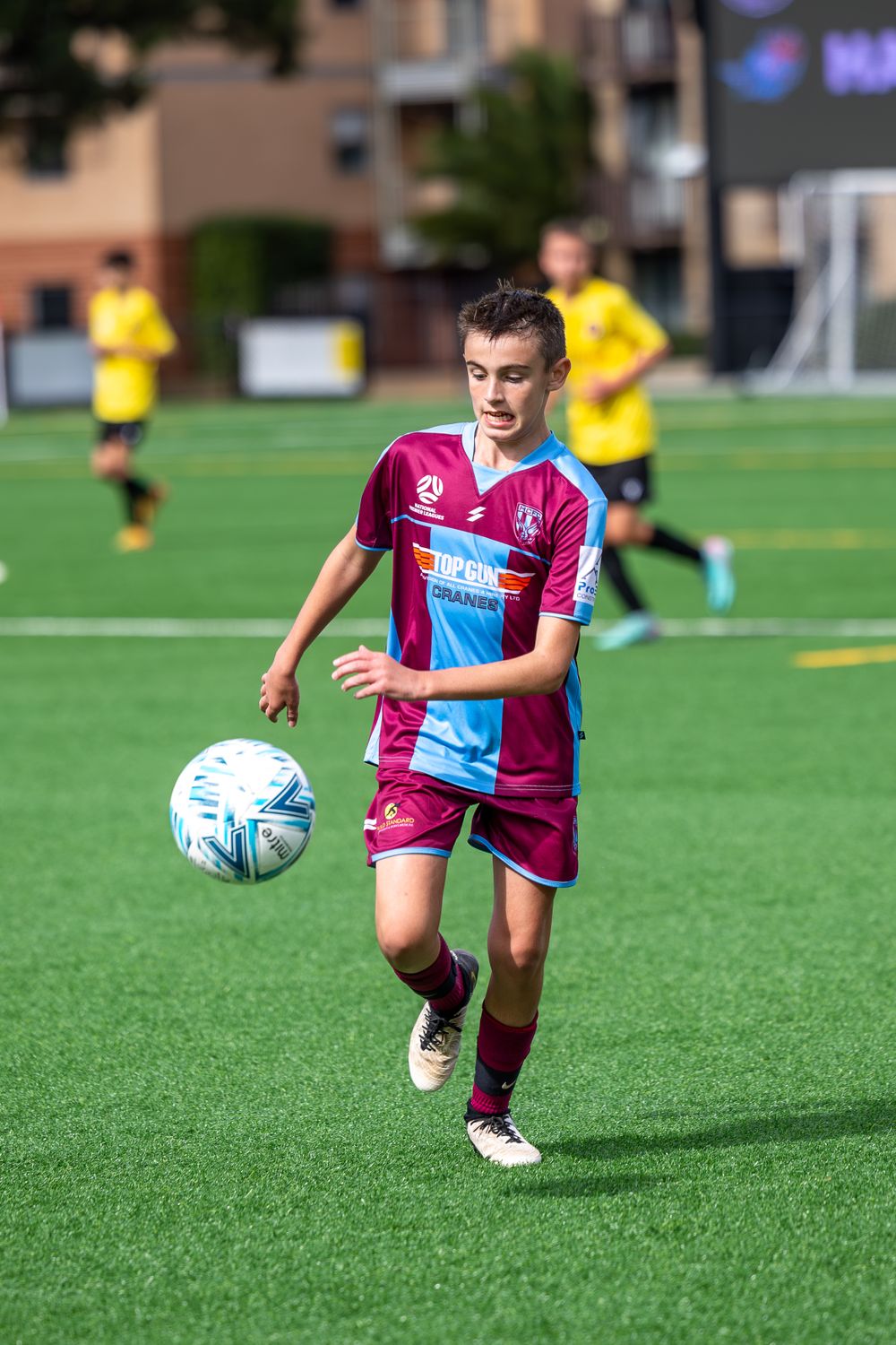 Soccer player in maroon and blue striped jersey dribbles ball during match.