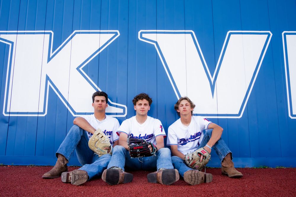 Three baseball players sitting against blue wall with large white letters.