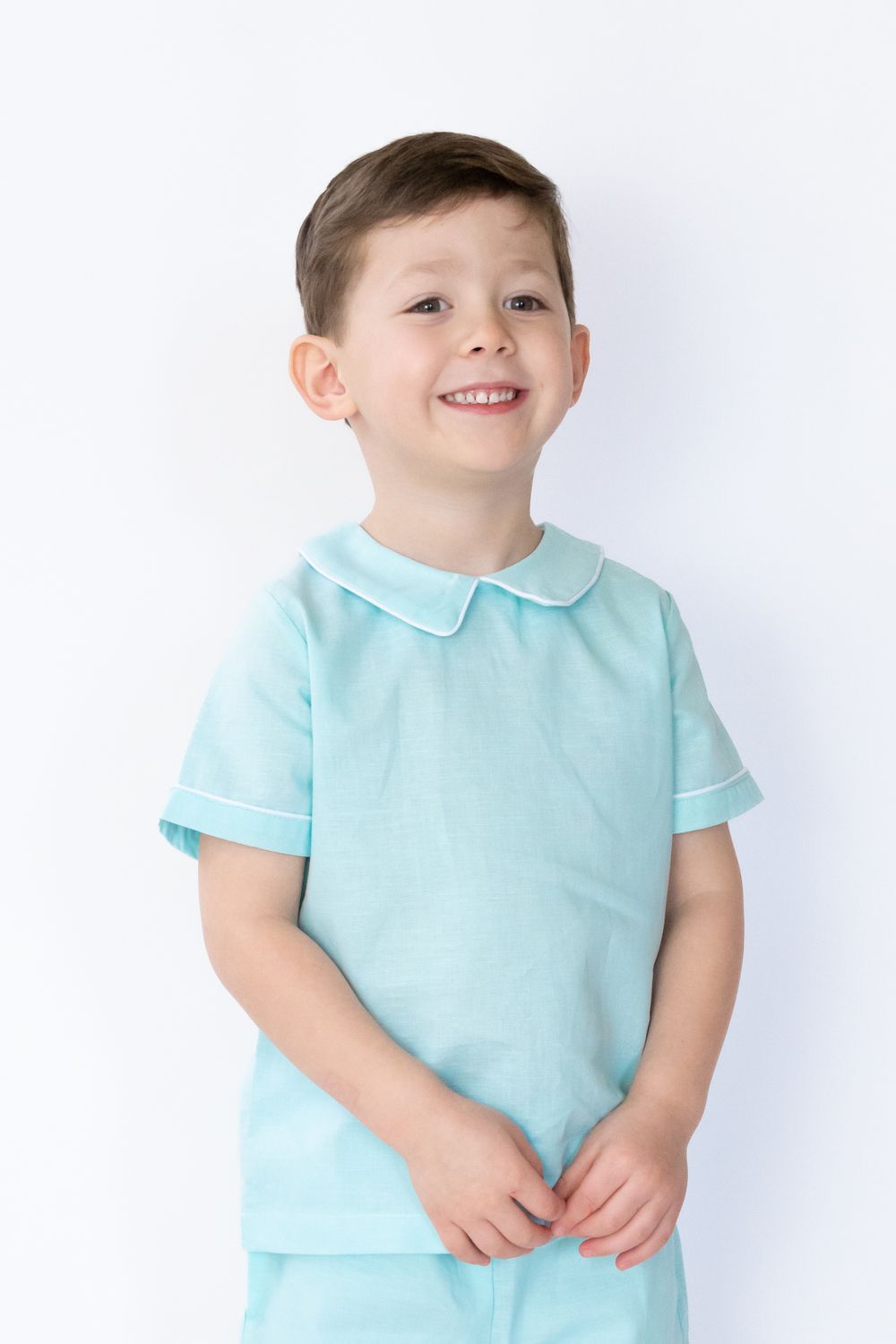 Young child wearing light blue collared shirt smiling against white background.