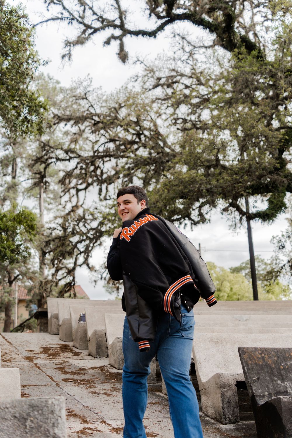 A person wearing a black hoodie stands by stone steps with mossy trees in the background.