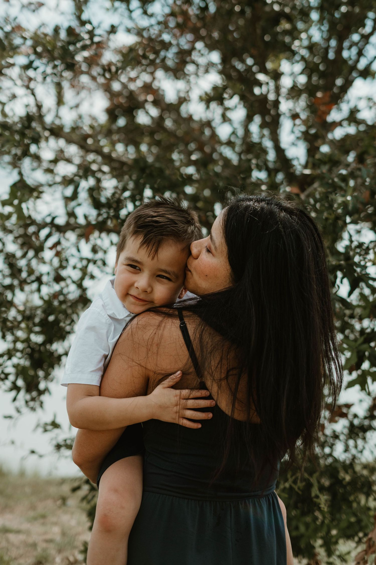 A tender moment between a parent and child embracing outdoors against a backdrop of trees.