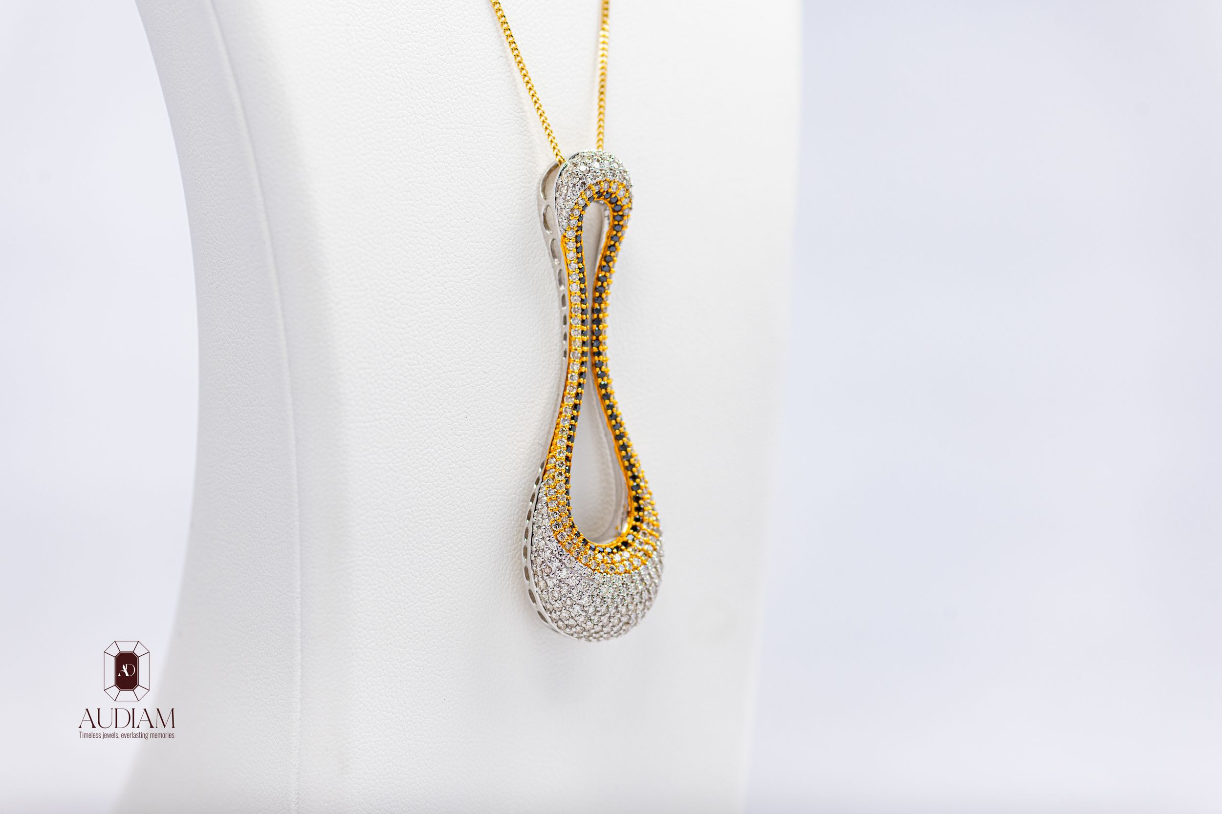 Gold and diamond infinity-shaped pendant necklace with pavé crystal detailing on a white jewelry display bust.