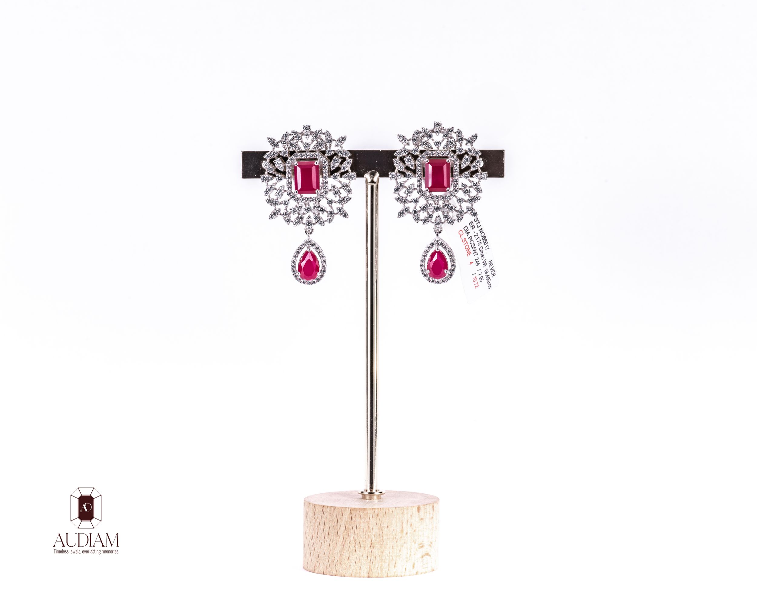 Elegant diamond and ruby drop earrings with floral design on display stand, featuring pink gemstone accents.