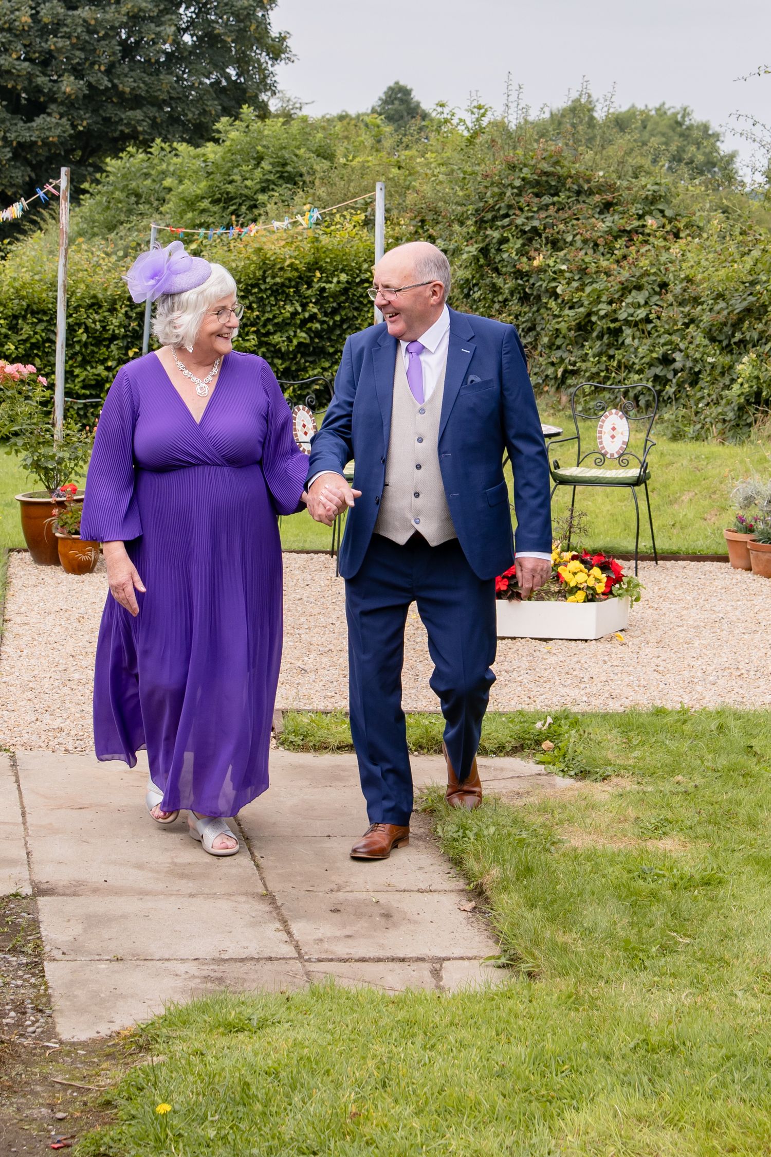 Wedding couple walking together through a garden path with blooming flowers.