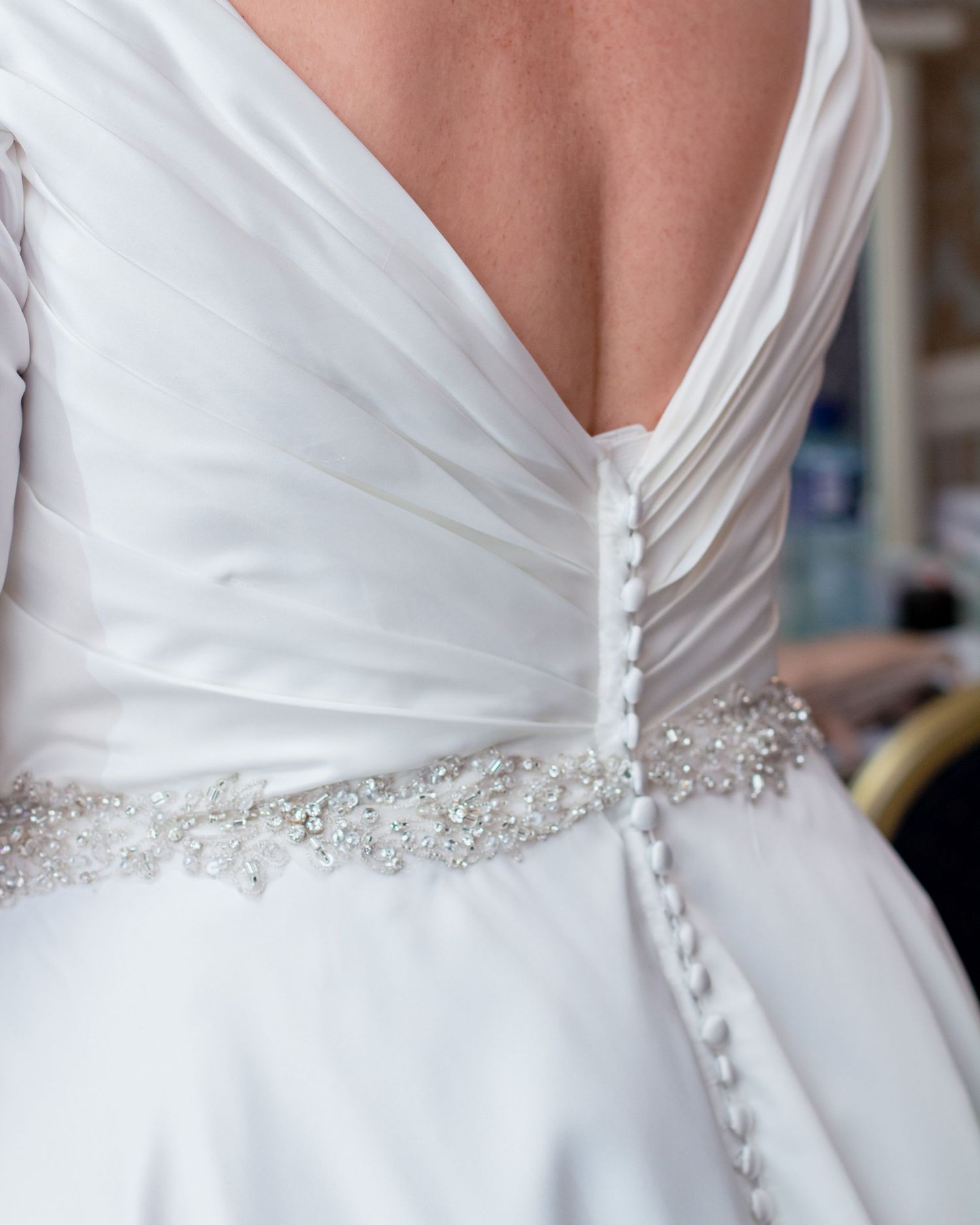 Close-up details of a white wedding dress with crystal beaded belt and button back closure.