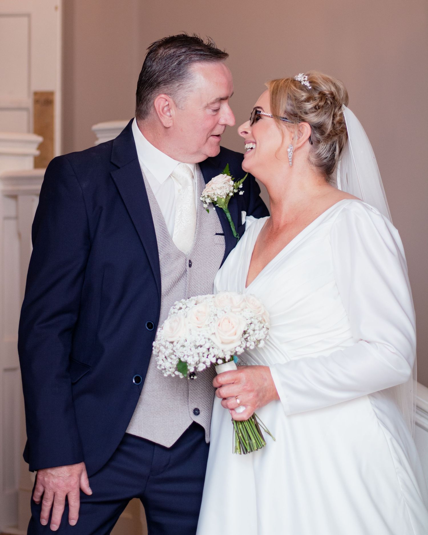 Wedding couple sharing intimate moments in formal attire against neutral indoor backdrop.