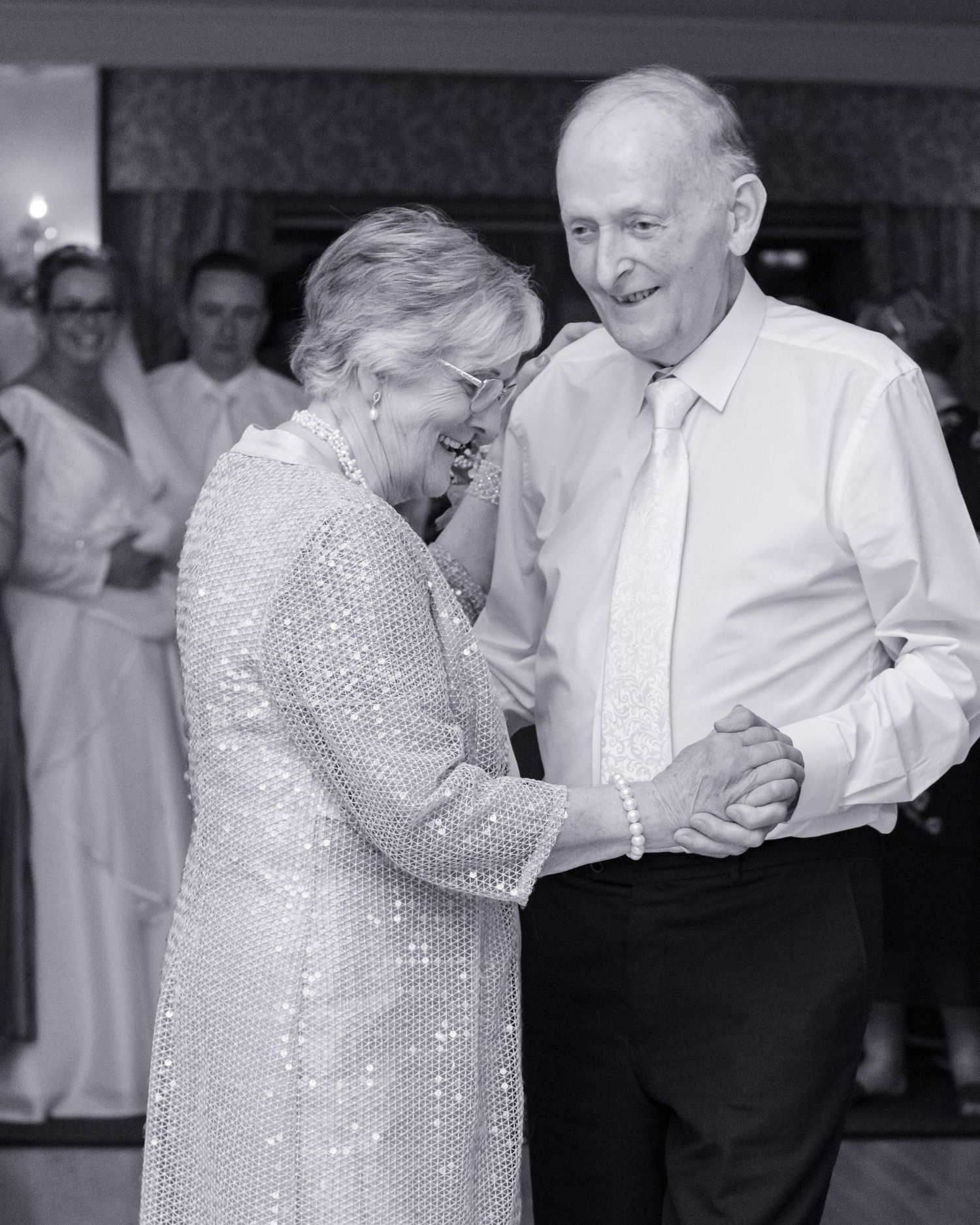 Couple dancing in formal attire at wedding reception in black and white photography.