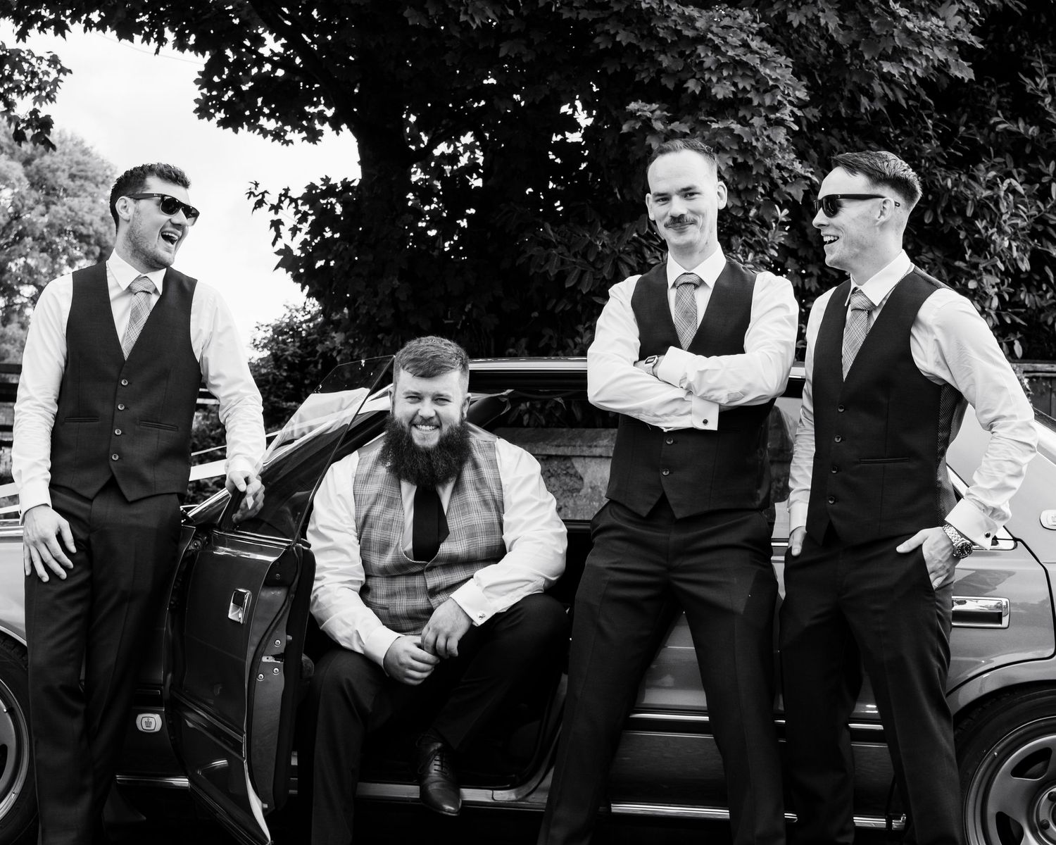 Group of groomsmen in formal attire posing casually outdoors.