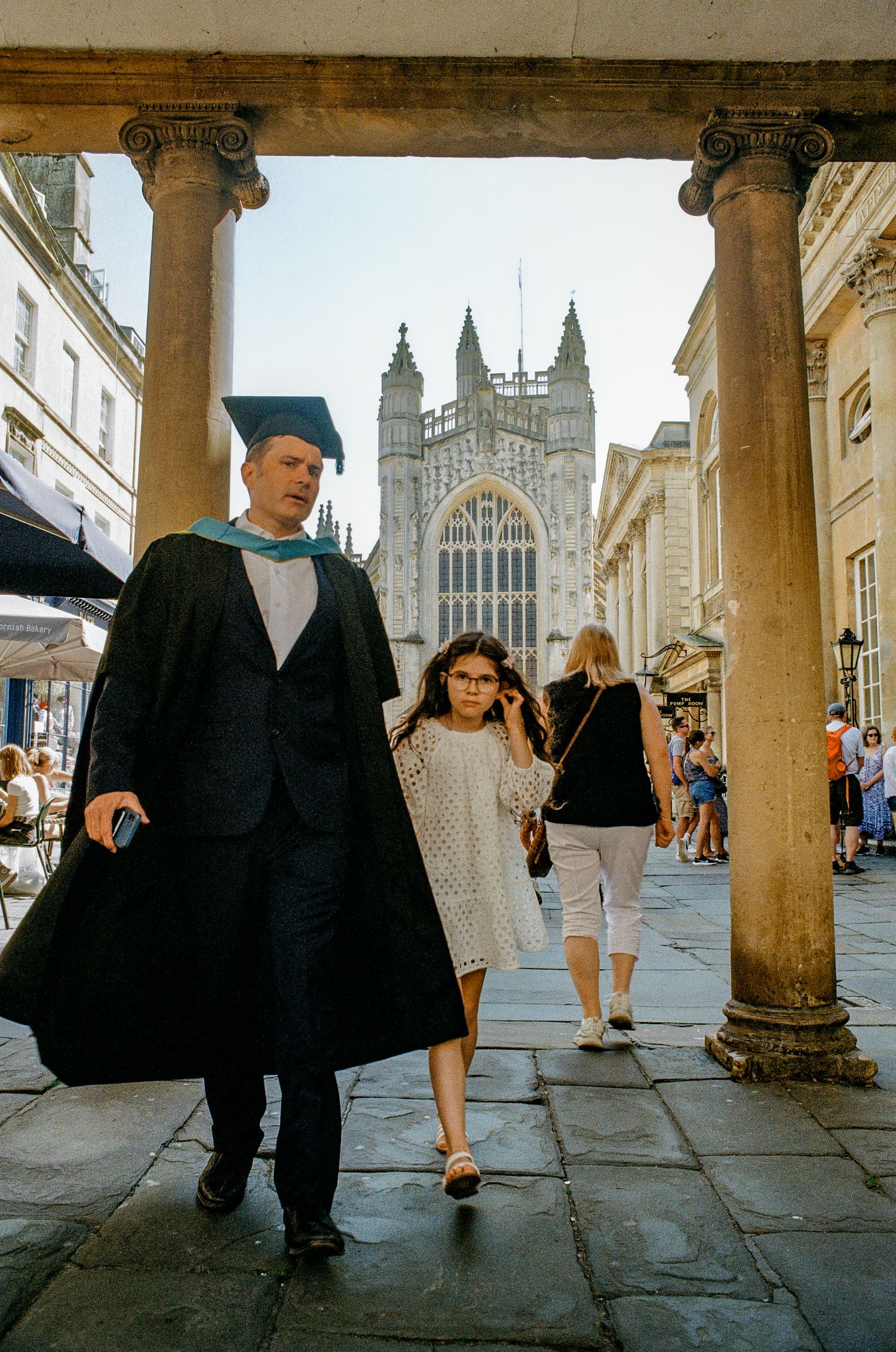 Bath Abbey's Gothic facade viewed through classical columns on a busy tourist street.