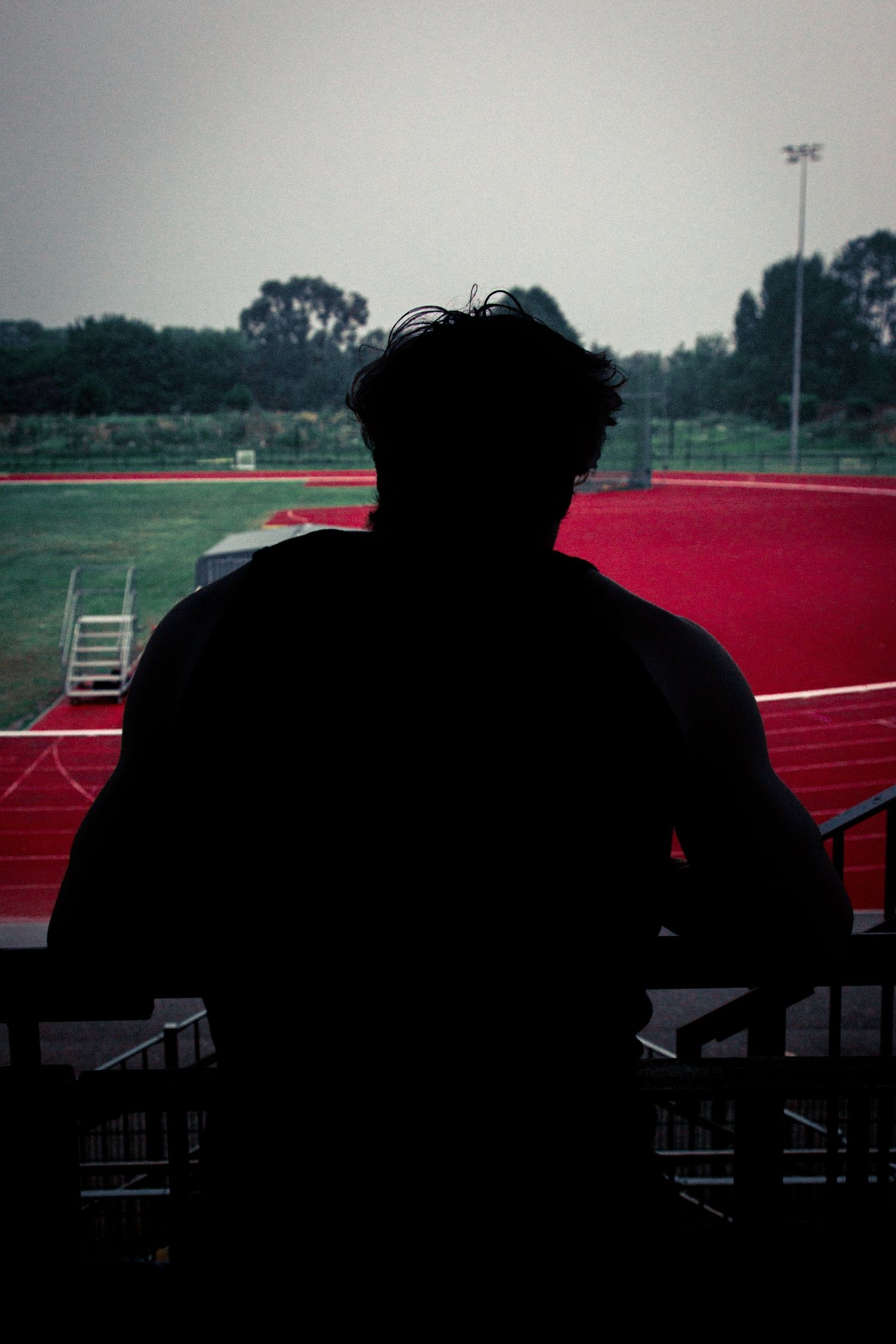 Silhouette overlooking red running track during overcast evening.