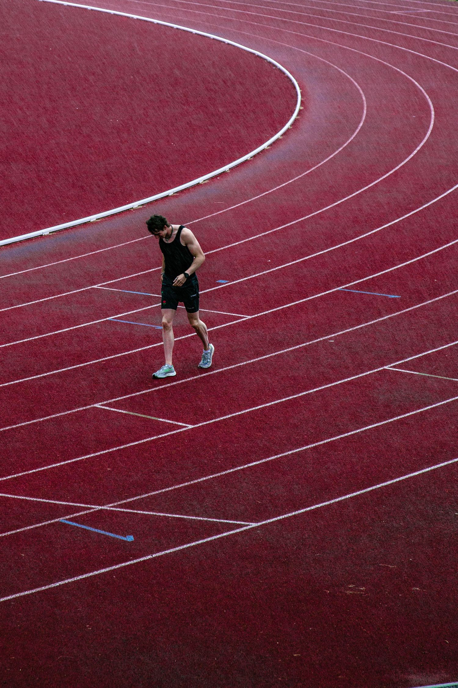 Empty red running track with white lane markings under dramatic lighting.