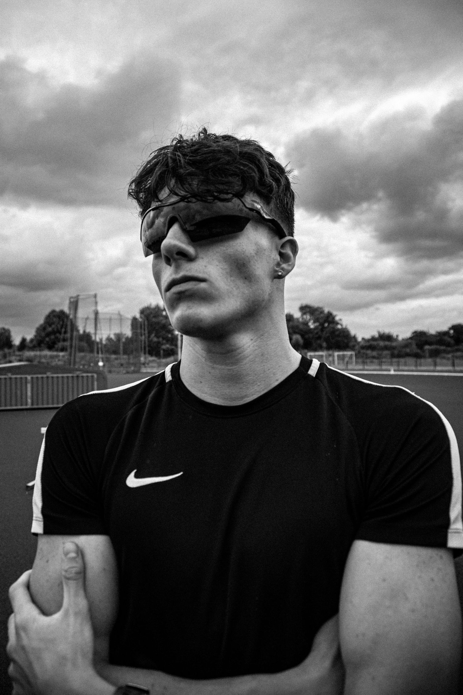 Athletic figure in black Nike shirt posing against dramatic cloudy backdrop.