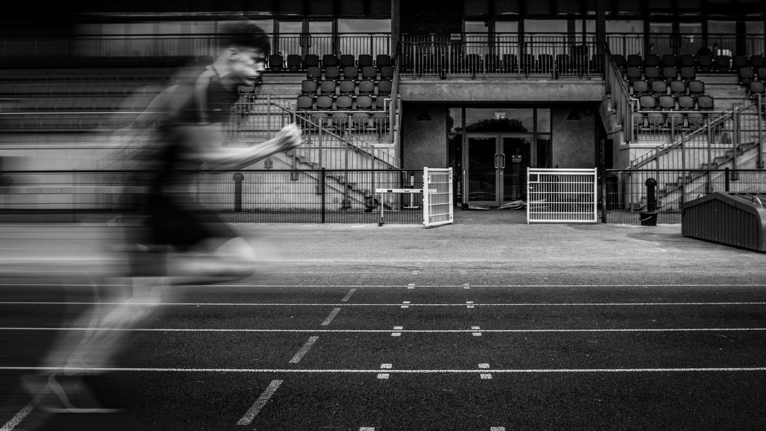 Empty stadium bleachers and track field in black and white monochrome.