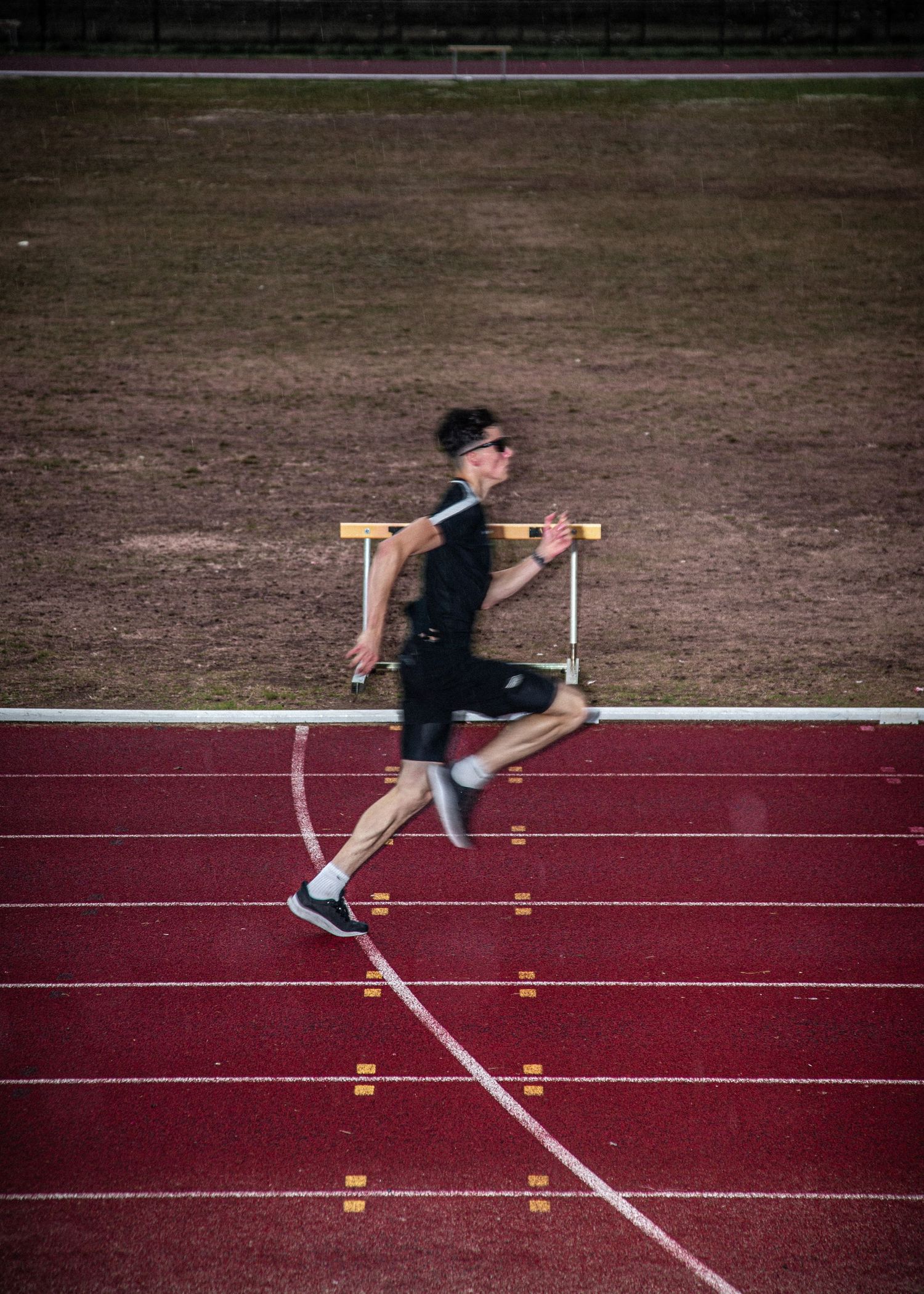 Runner practicing hurdles technique on red running track with markers.