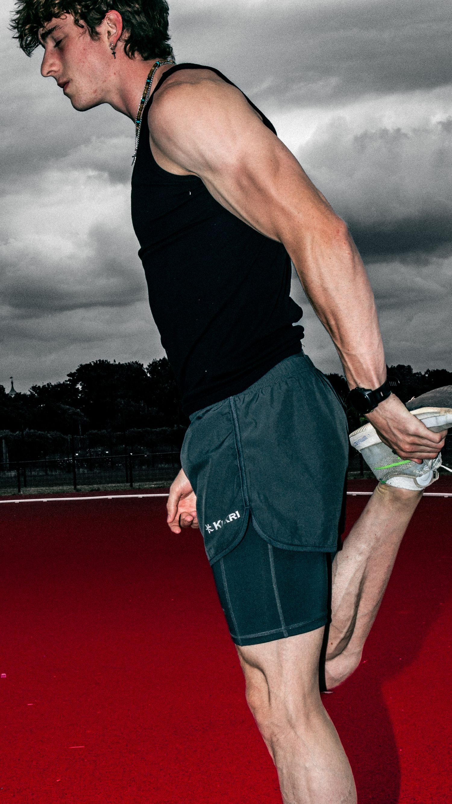 Close-up of an athlete stretching in black athletic wear against stormy skies.