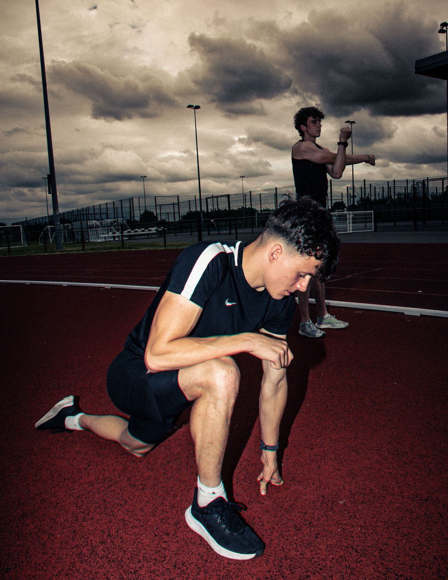 Athlete stretching on red track surface under stormy sky.