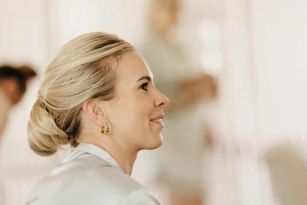 Side profile view of a bride wearing pearl earrings and an elegant updo hairstyle during wedding preparations.
