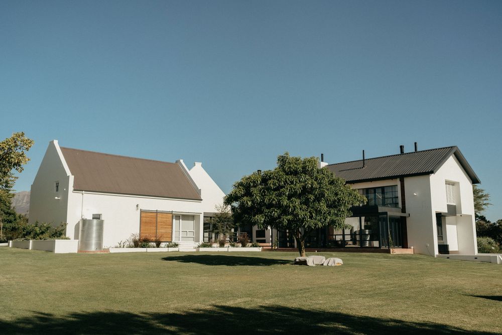 Two modern farmhouse-style buildings with white exteriors stand on a green lawn under a clear blue sky.
