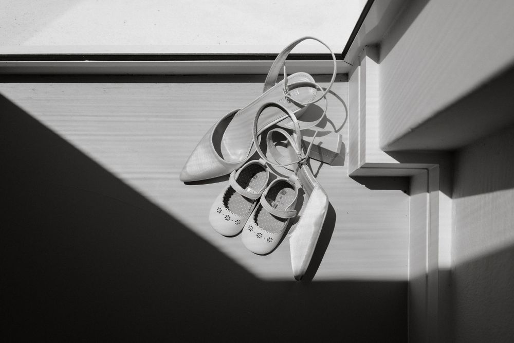 Wedding sandals cast dramatic shadows on a white surface in black and white photography.