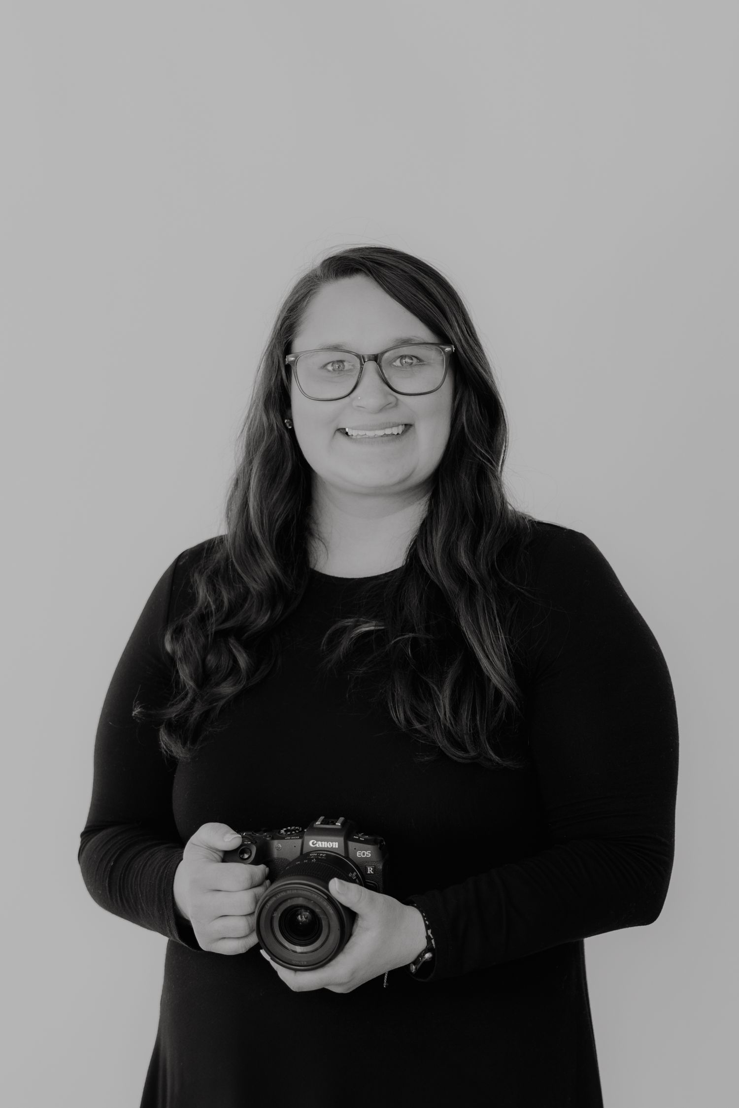 Professional photographer wearing glasses and black sweater holding camera in studio.
