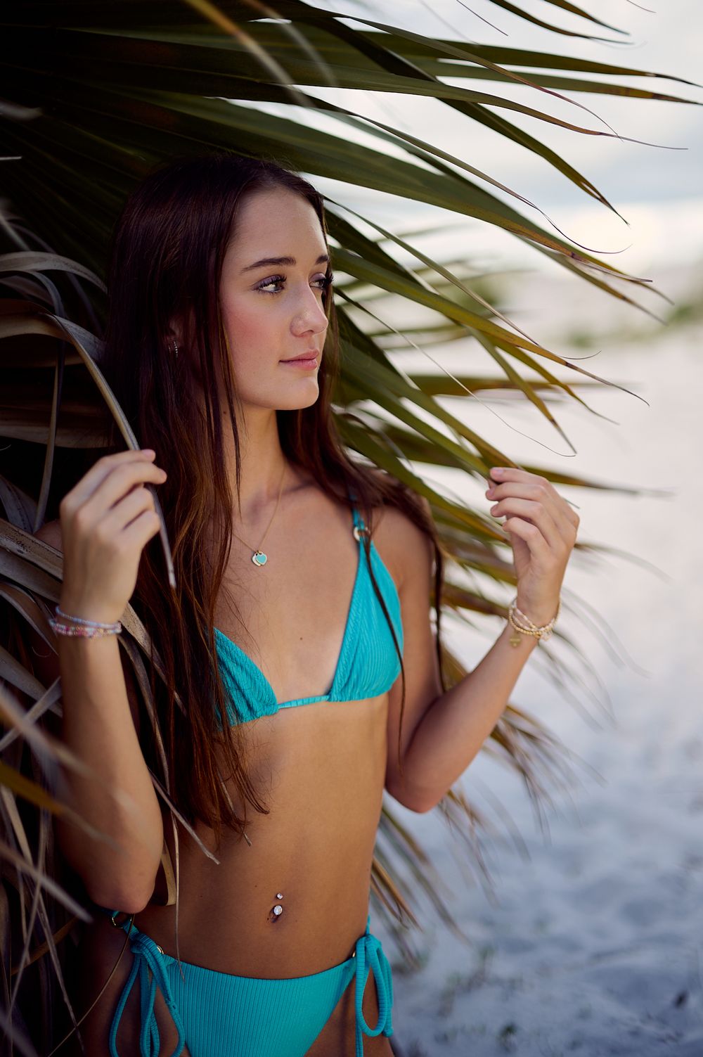 Woman in turquoise swimsuit poses artistically near palm fronds at the beach in sequential lifestyle photos.