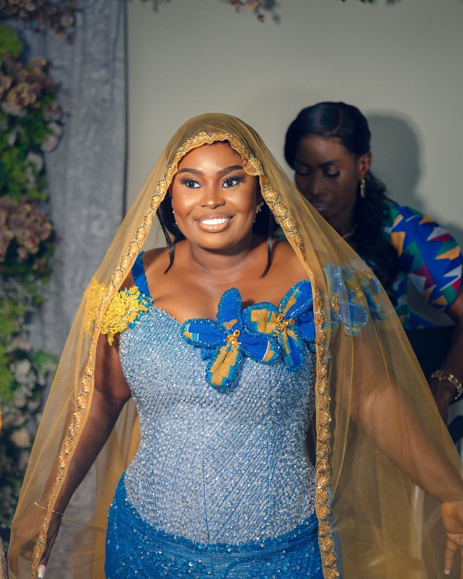 Person in sparkling blue gown and gold veil poses at formal celebration.