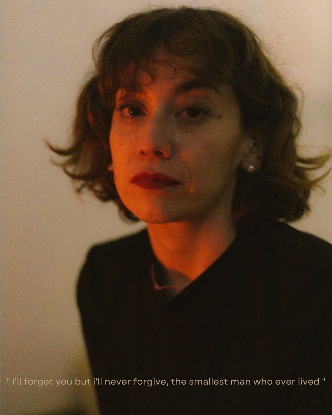 Woman with short auburn hair and red lips in dramatic orange lighting wearing black top with emotional quote overlay.