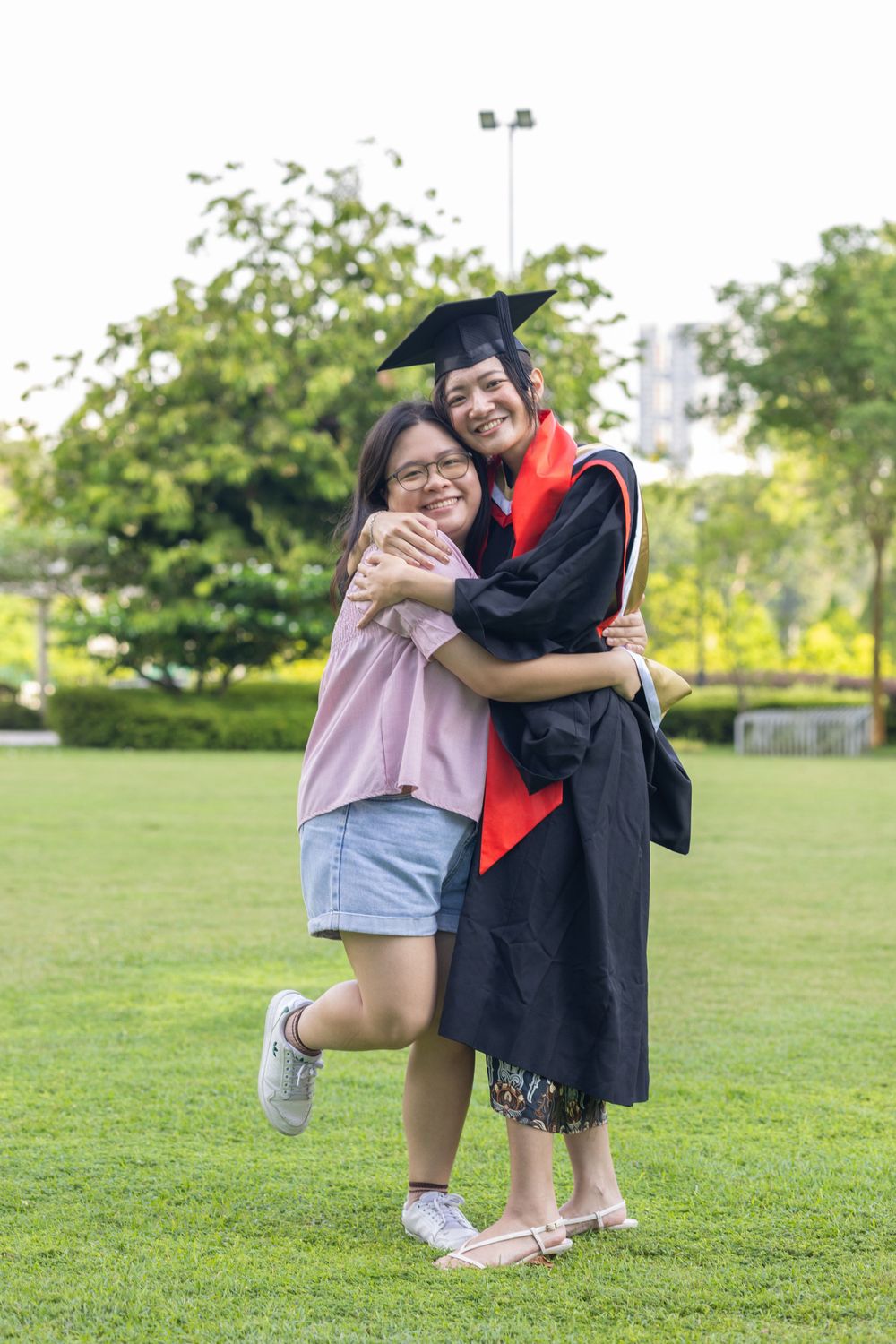 Two people share celebratory hug on grassy lawn during graduation festivities.