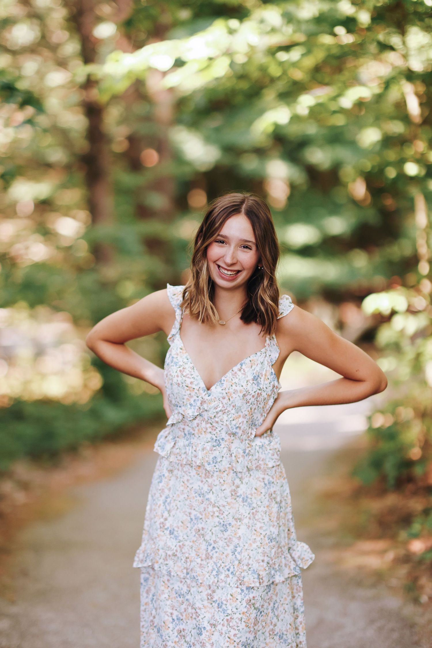 Woman in floral summer dress poses on forest path during golden hour.