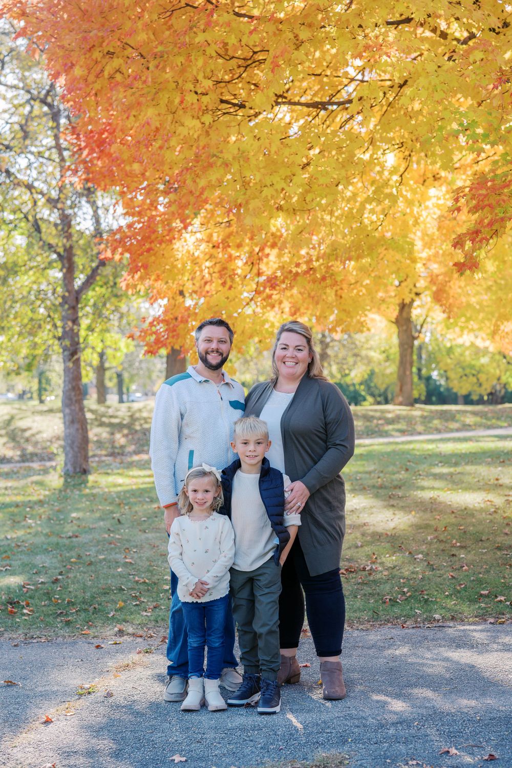 A family portrait captured under vibrant orange and yellow autumn trees.