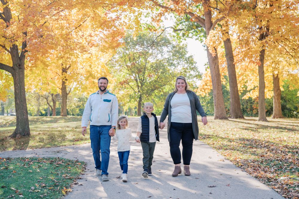 People walking together on a tree-lined path during autumn with golden leaves overhead.
