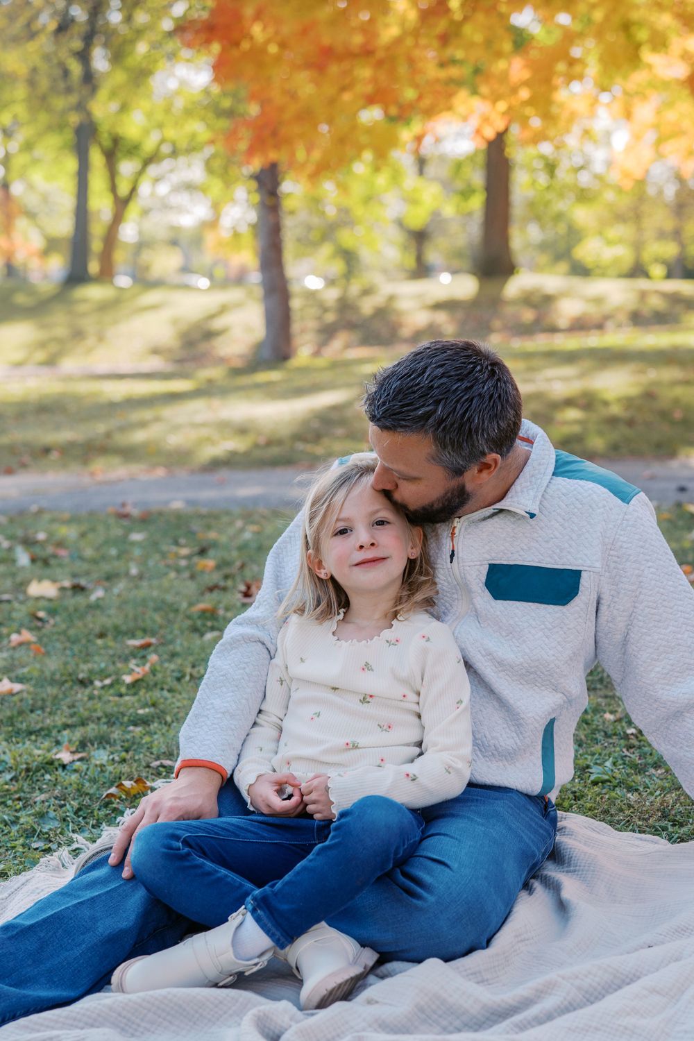 Tender moment shared while sitting on blanket under fall foliage.